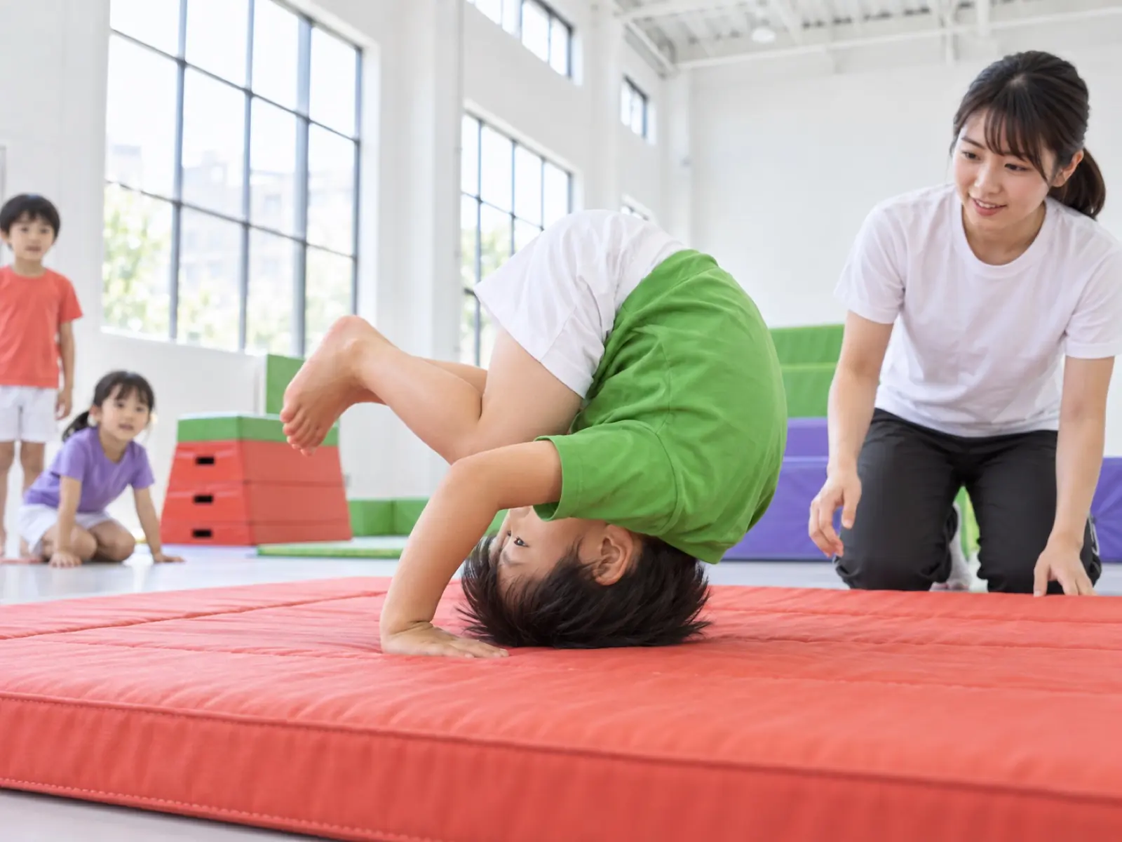 マットで前まわりをする子と、横で見守る先生